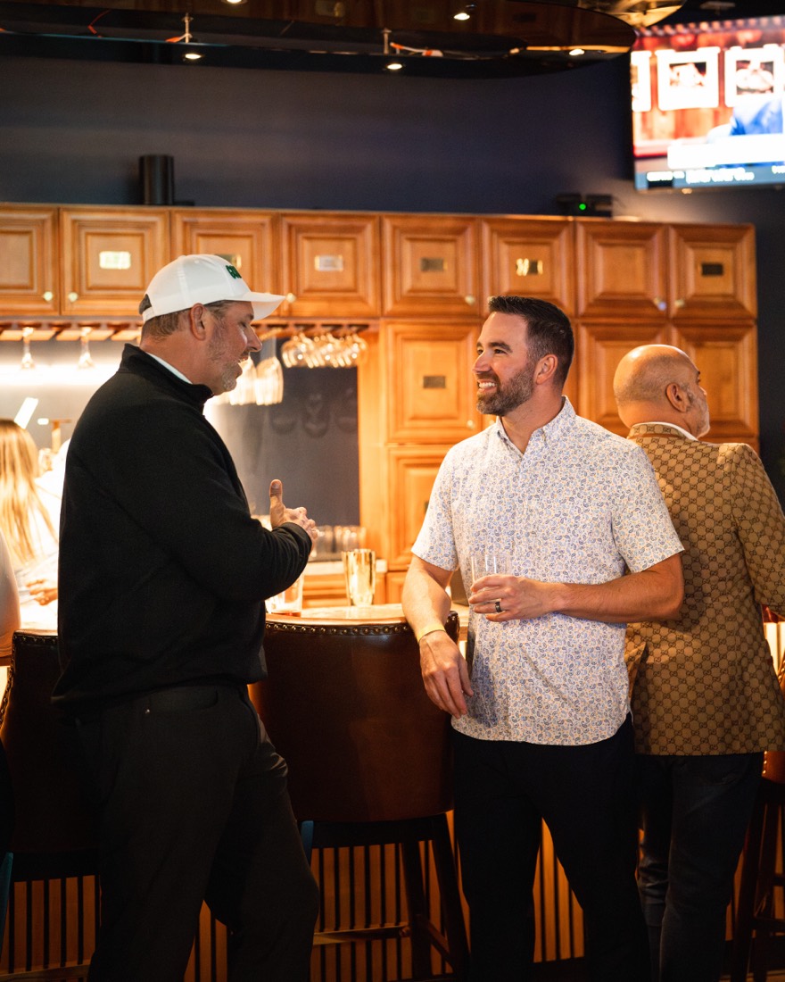 Two members talking at the bar in front of the liquor cabinets